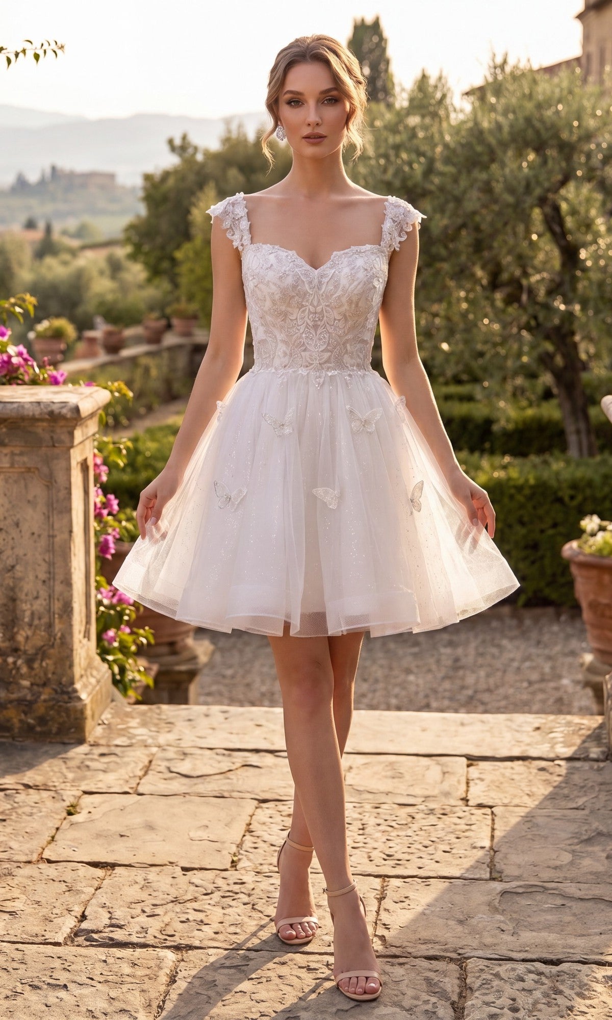 A woman wearing the Short Homecoming Dress: Chicas C330 in off white, featuring floral lace appliques and cap sleeves, stands outdoors on a stone path surrounded by greenery and flowers.